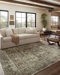 a living room with a couch, chair and rug on the floor in front of large windows