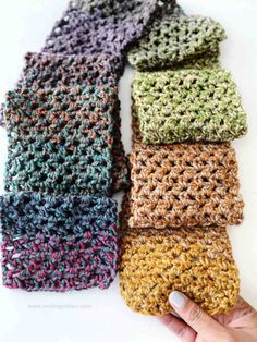 four crocheted dishcloths in different colors on a white surface with a hand holding