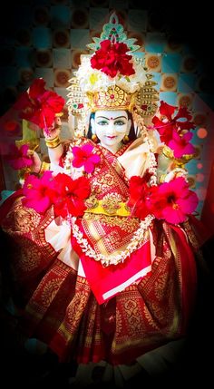 a woman dressed in red and gold with flowers on her head, wearing a mask