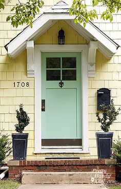 the front door of a yellow house with two planters