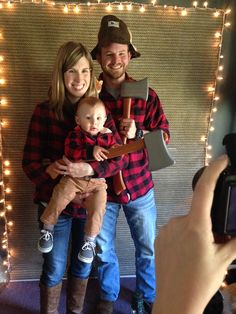 a man and woman holding a baby in front of a christmas light display with lights behind them