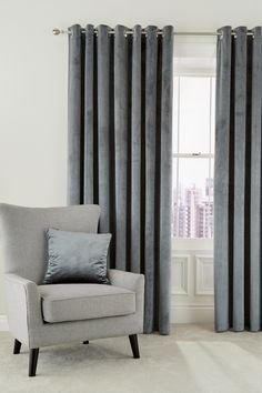 a gray chair sitting in front of a window covered in black and white striped curtains