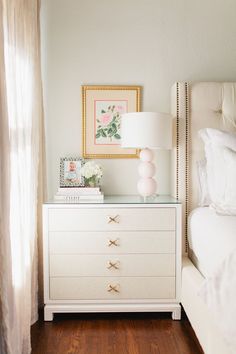 a white dresser sitting next to a bed with a lamp and pictures on top of it