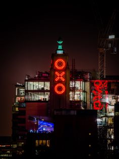 an illuminated clock tower in the middle of a city at night with buildings and lights behind it