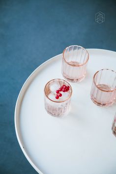 three shot glasses on a white plate with some red berries in the middle and one glass filled with water