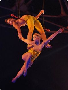 two people are performing aerial acrobatic tricks in the air with one holding on to another