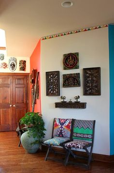 two chairs and a potted plant in front of a wall with pictures on it