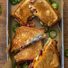 two grilled sandwiches in a pan with green peppers on the side and one cut in half