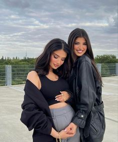 two women standing next to each other in front of a parking lot with cloudy skies