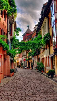 an alley way with buildings and trees on both sides, surrounded by cobblestones