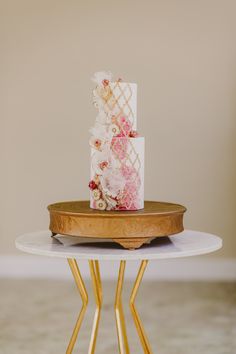 a table topped with a white cake covered in pink and yellow flowers on top of a wooden stand