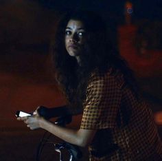 a woman with long hair riding a bike at night holding a cell phone in her hand