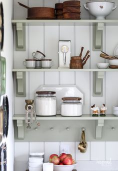 the shelves are filled with dishes and utensils, including an apple in a bowl