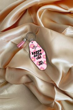 a pink and white keychain with the word aloha on it sitting on a satin surface