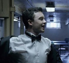 a man wearing a white shirt and black bow tie standing in a room with other people