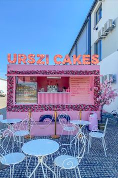 a pink ice cream cart sitting on top of a street next to tables and chairs