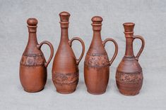 four brown vases are lined up in a row on a gray surface, one is empty and the other has an intricately decorated handle