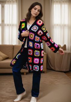 a woman standing in front of a couch wearing a colorful crochet coat