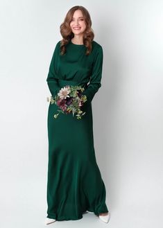 a woman in a long green dress with flowers on her waist and hands behind her back