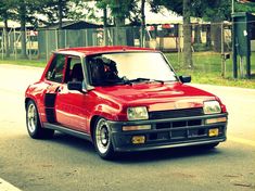 a red car is parked on the side of the road in front of a fence