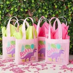 three pink and green bags with dinosaurs on them sitting next to each other in front of some bushes