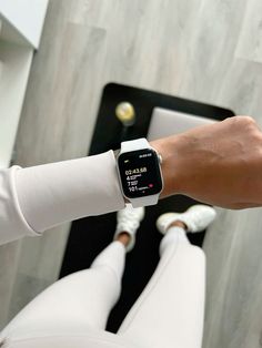 a person wearing an apple watch on their wrist with white pants and sneakers in the background