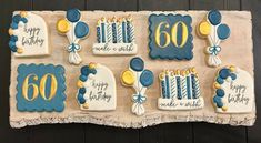 a birthday cake decorated with blue and yellow icing on a wooden table next to a sign that says happy 60th