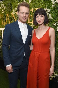 a man and woman standing next to each other in front of a wall with flowers