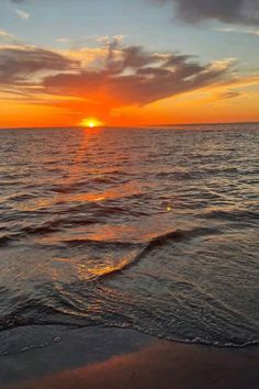 the sun is setting over the ocean with waves coming in to shore and some clouds