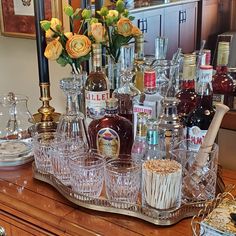 an assortment of liquor bottles and glasses sitting on a wooden table with flowers in vases