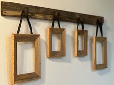 three wooden frames hanging on a wall with black cords attached to the hooks and one is holding two small square ones