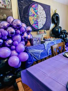 purple and black balloons are on the table in this party room with blue cloths