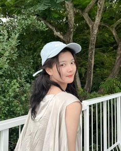 a woman standing on a porch next to trees and wearing a white top with a blue hat