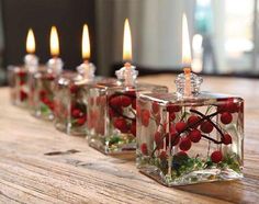 small glass candles with berries in them on a wooden table next to other candles and flowers