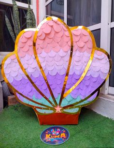 a large pink and purple kite sitting on top of a lush green field next to a window