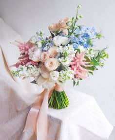 a bridal bouquet with pink, white and blue flowers on a bed sheet in front of a wall