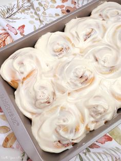 a pan filled with frosted cinnamon rolls on top of a table