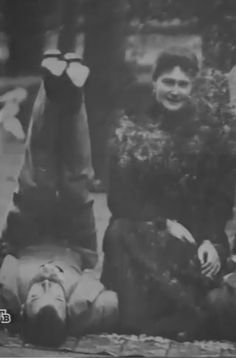 an old black and white photo of two women sitting on the ground with one woman laying down