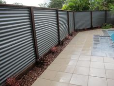 a long fence next to a swimming pool in a backyard with stone pavers flooring