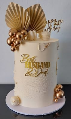 a white and gold birthday cake on a black table with some decorations around the top