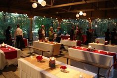 people standing around tables with red and white tablecloths on them, surrounded by lights