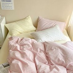 an unmade bed with pink and white checkered comforter, pillows and sheets