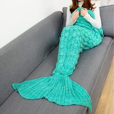 a woman sitting on top of a couch covered in a green mermaid tail knitted blanket