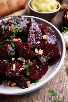 a white plate topped with beets and nuts next to other foods on a wooden table