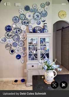 a white china cabinet sitting next to a vase filled with blue and white plates on top of a wall