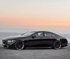 a black car parked on top of a dry grass field next to the ocean at sunset