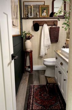 a white toilet sitting in a bathroom next to a wooden cabinet and rug on top of a hard wood floor