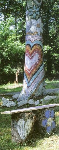 a tree that has been painted with hearts on it and is next to a bench