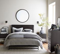 a bed room with a neatly made bed and a round mirror on the wall above it