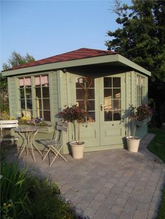 a small green shed sitting on top of a brick patio next to a table and chairs